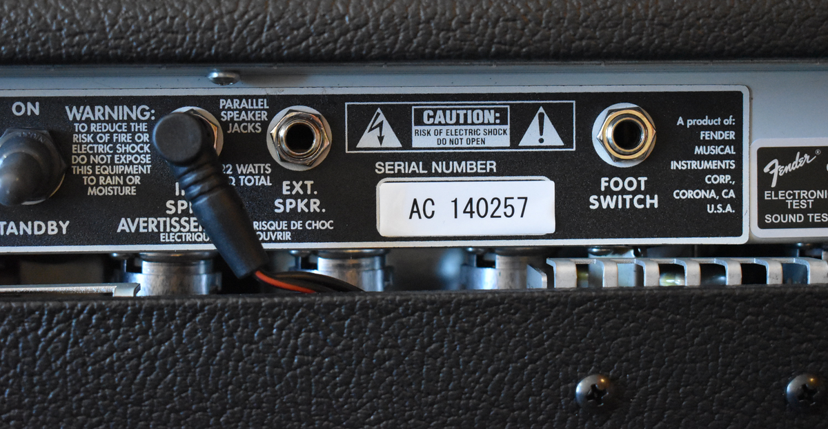 Close-up of the amp's black rear panel, showing the serial number AC 140257, speaker jacks, and a connected black cable.