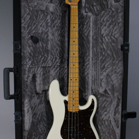 Full front view of a white bass guitar with a tortoiseshell pickguard, maple neck, and chrome hardware, resting in a grey plush-lined hard case.