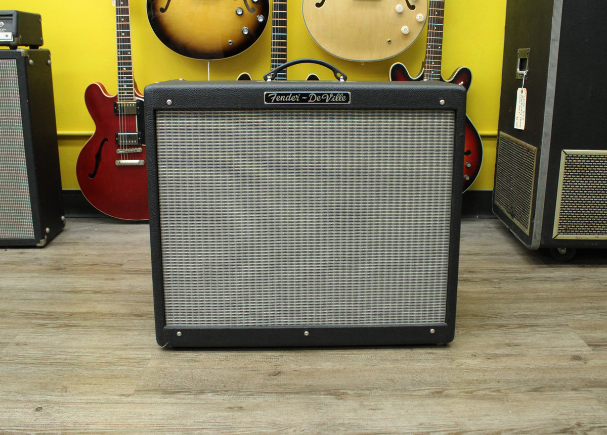 Front view of a black combo amp with a silver grille, black handle, and a silver badge on the top front.