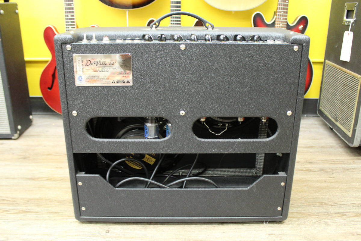 Rear view of a black textured combo amp, showing exposed tubes and speakers through two upper and one lower cutout.
