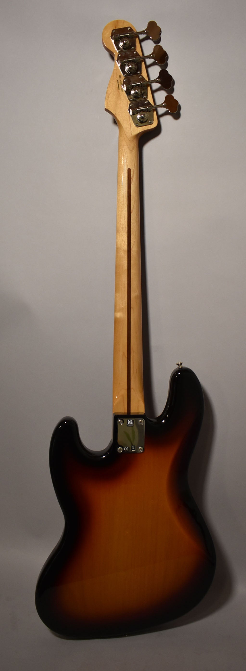 Full rear view of a sunburst bass, showing the glossy body, light wood neck, and four gold-colored tuners.