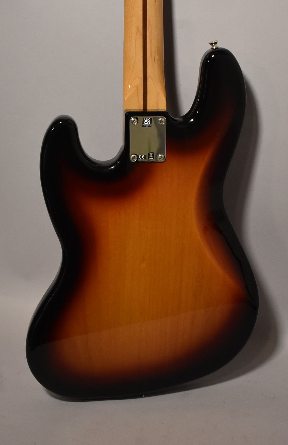 Rear view of a sunburst Jazz Bass, showing the glossy body, maple neck, and chrome neck plate with a strap button.