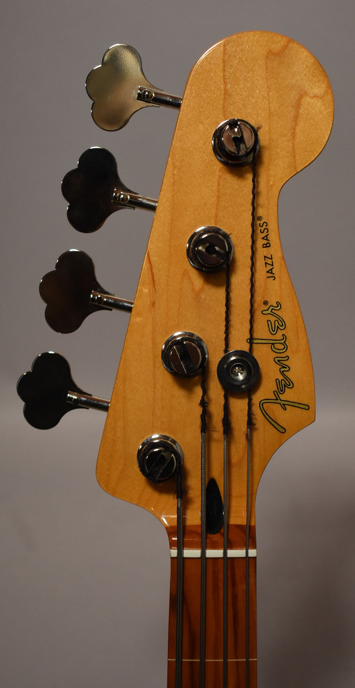 Close-up of the bass headstock, showing the light wood finish, four chrome tuners, and dark fretless fingerboard.