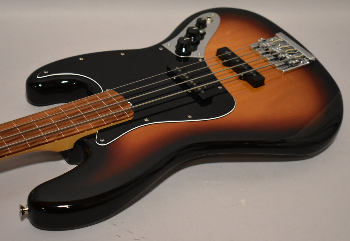 A sunburst fretless Jazz Bass, angled from the lower left, showing the body, black pickguard, and rosewood fingerboard.