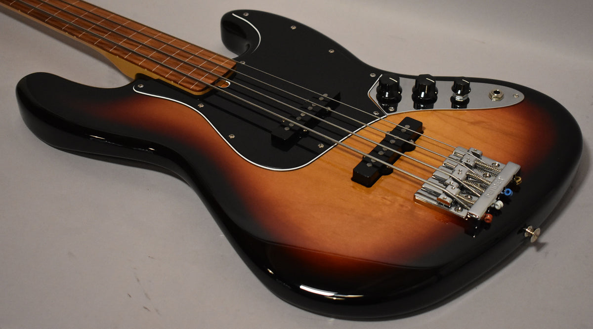 Sunburst fretless bass, angled from the neck to the lower body, showing the black pickguard, chrome bridge, and control plate.