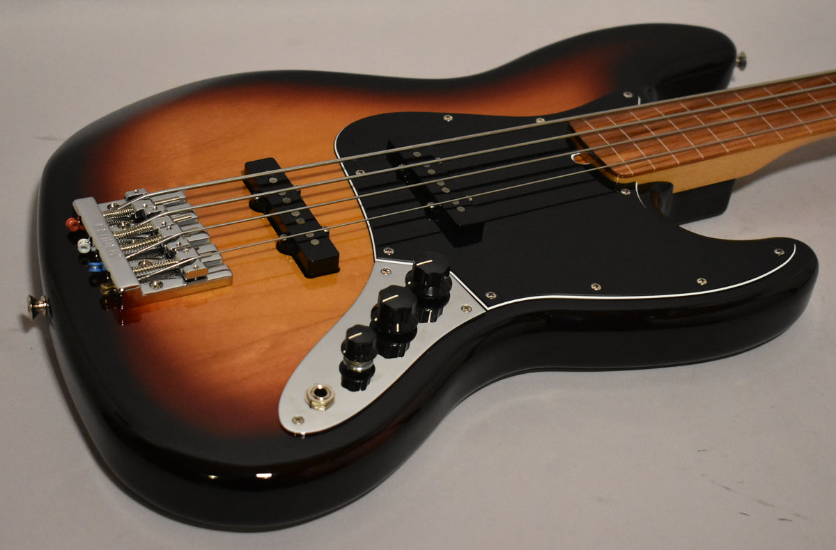 Sunburst Jazz Bass body, angled from above, showing the black pickguard, chrome bridge, and three black control knobs.