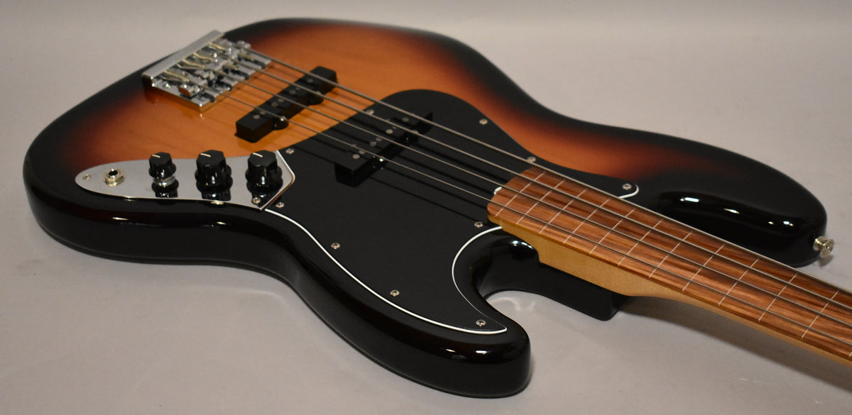 View 10 of 20: A sunburst fretless bass, angled from the lower bout, showing its black pickguard, chrome control plate, and four black knobs.