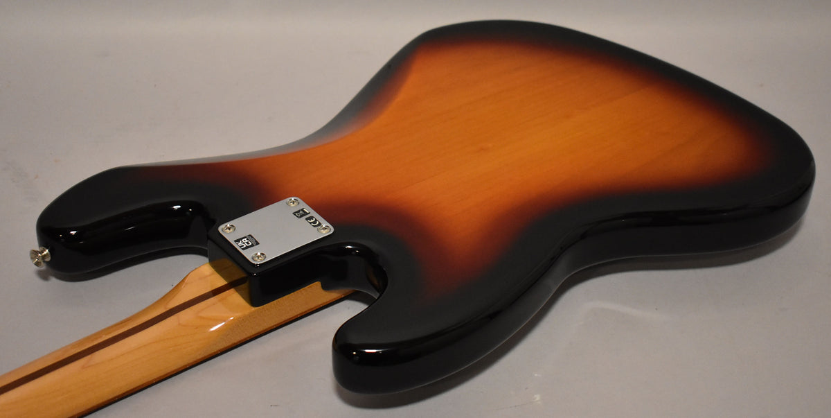The back of a sunburst Jazz Bass body, showing the neck plate, strap button, and a maple neck with a dark stripe.
