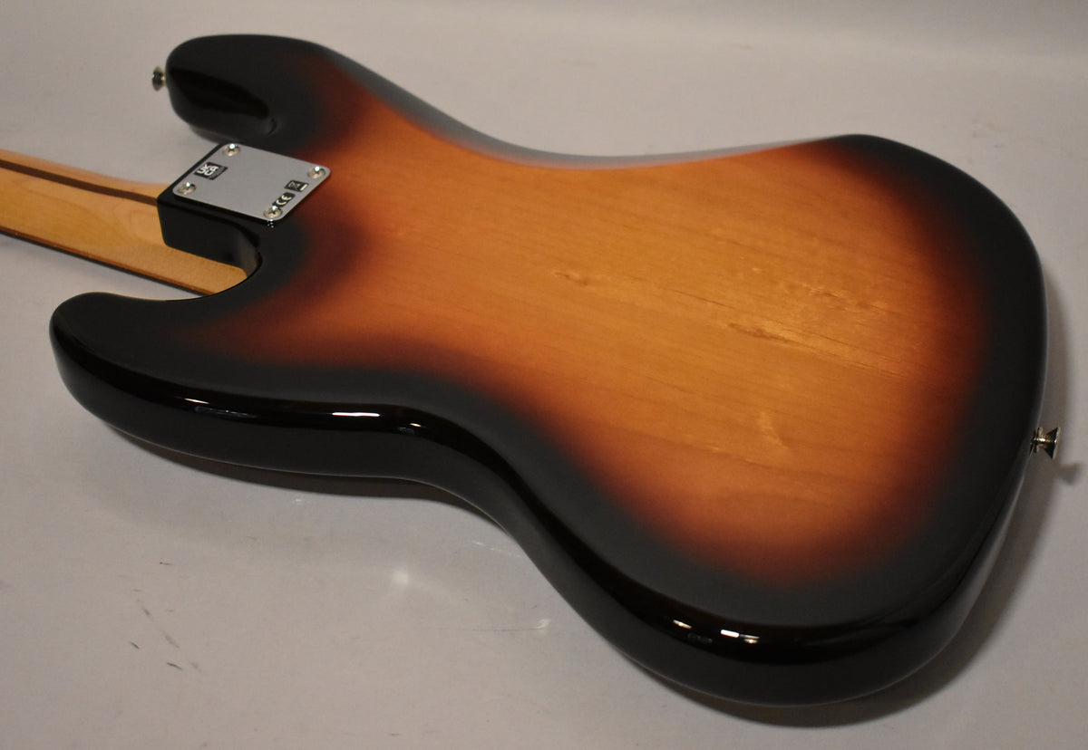 The bass guitar's sunburst body, with a glossy finish, is viewed from the back, showing the neck plate and a strap button.