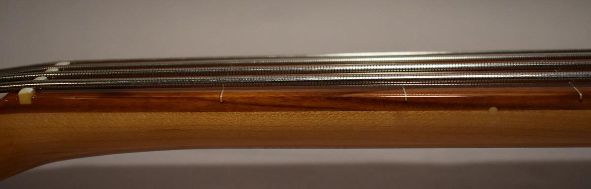 Close-up of the bass neck from the nut to the 7th position, showing the light wood neck, dark fretboard, and four strings.
