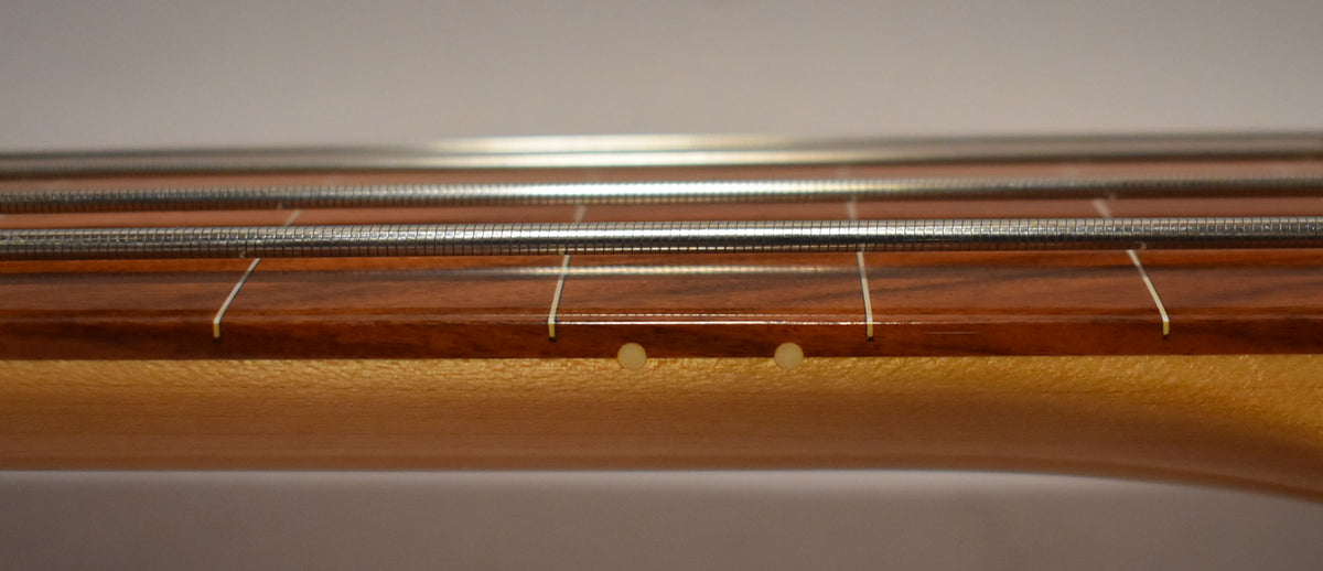 Close-up of the bass's fretless rosewood fingerboard with white fret lines and two light-colored side dots.
