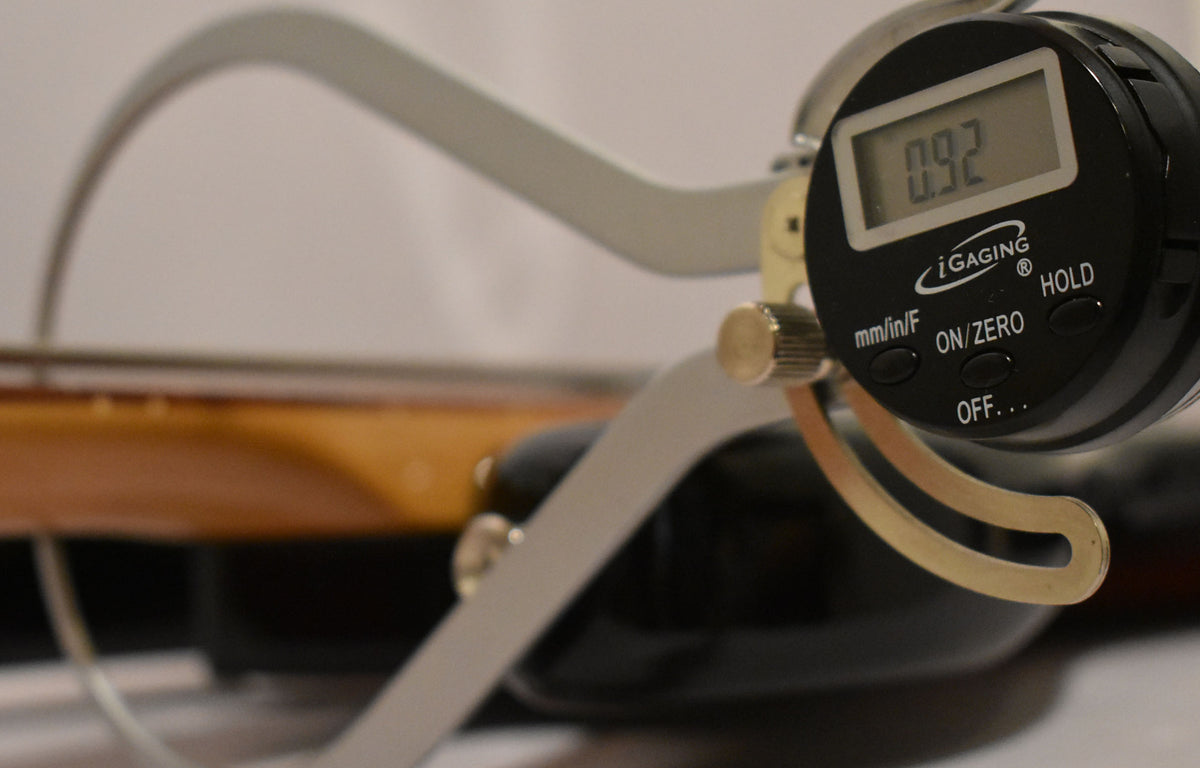 Close-up of a digital caliper measuring the fretless neck of the sunburst bass, showing a reading of 0.92.