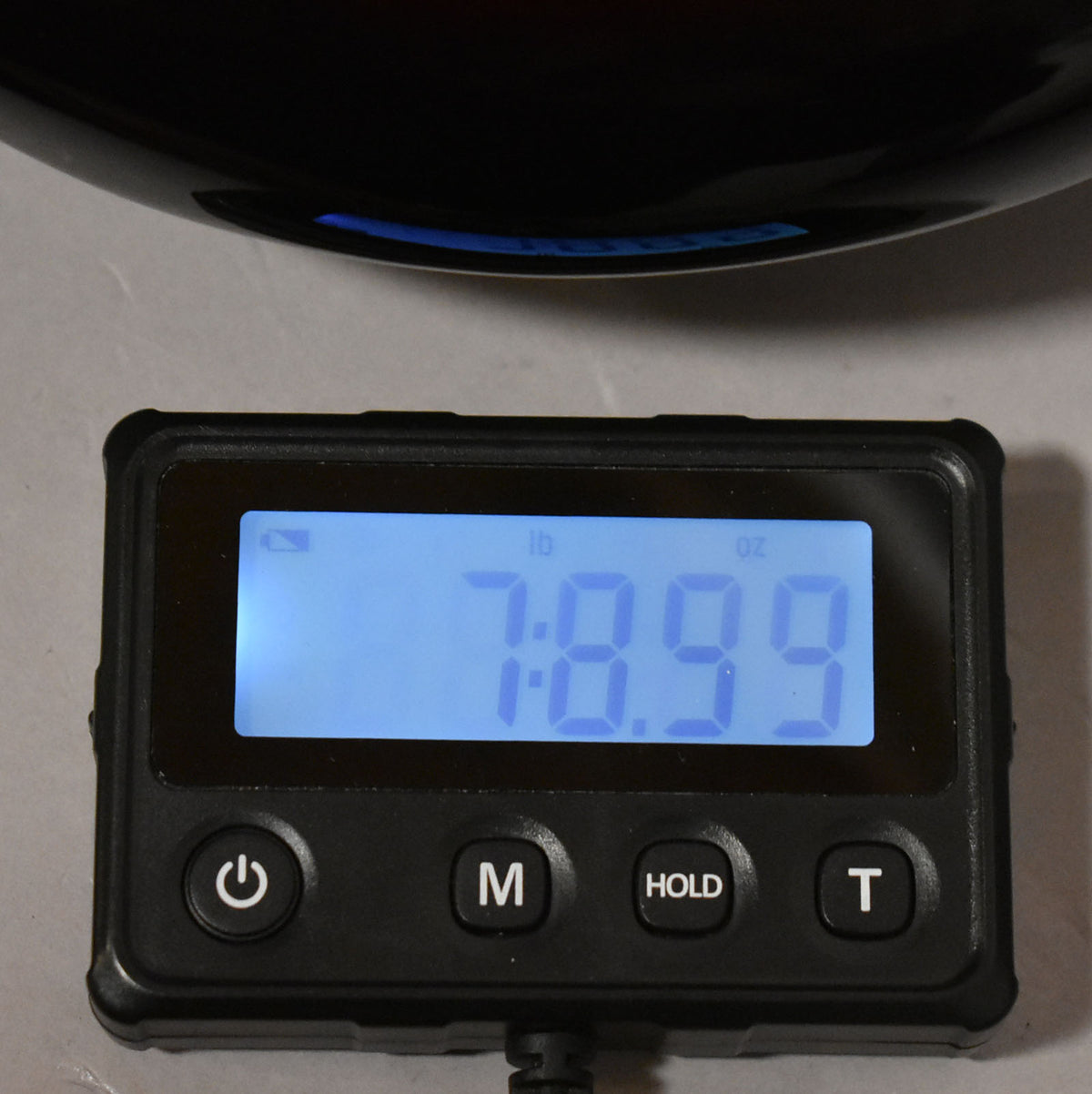 A close-up of a digital scale displaying "7 lb 8.99 oz" with a sunburst bass body partially visible above.