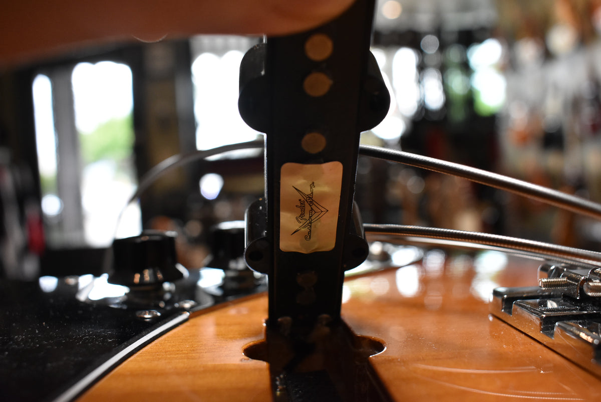 Close-up of the bass's sunburst body and black pickguard, showing a control knob and the bridge with four strings.