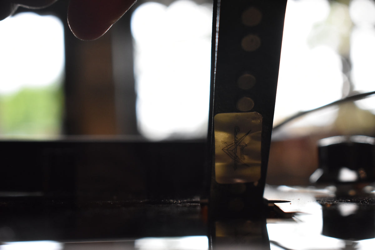 Close-up of the bass's dark fretboard and body, showing a worn gold sticker with a stylized figure near a control knob.