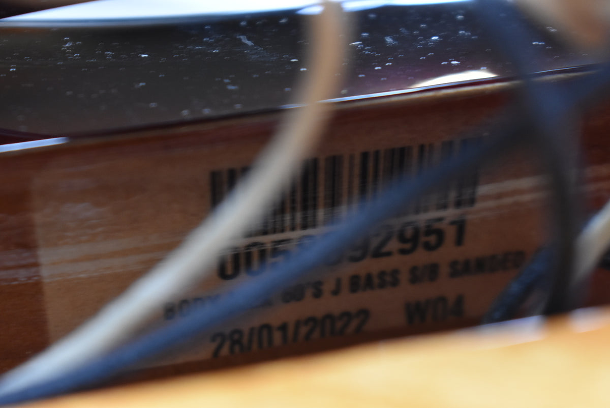 Close-up of the bass's body cavity, revealing a barcode sticker with "005892951" and "28/01/2022" visible through wiring.
