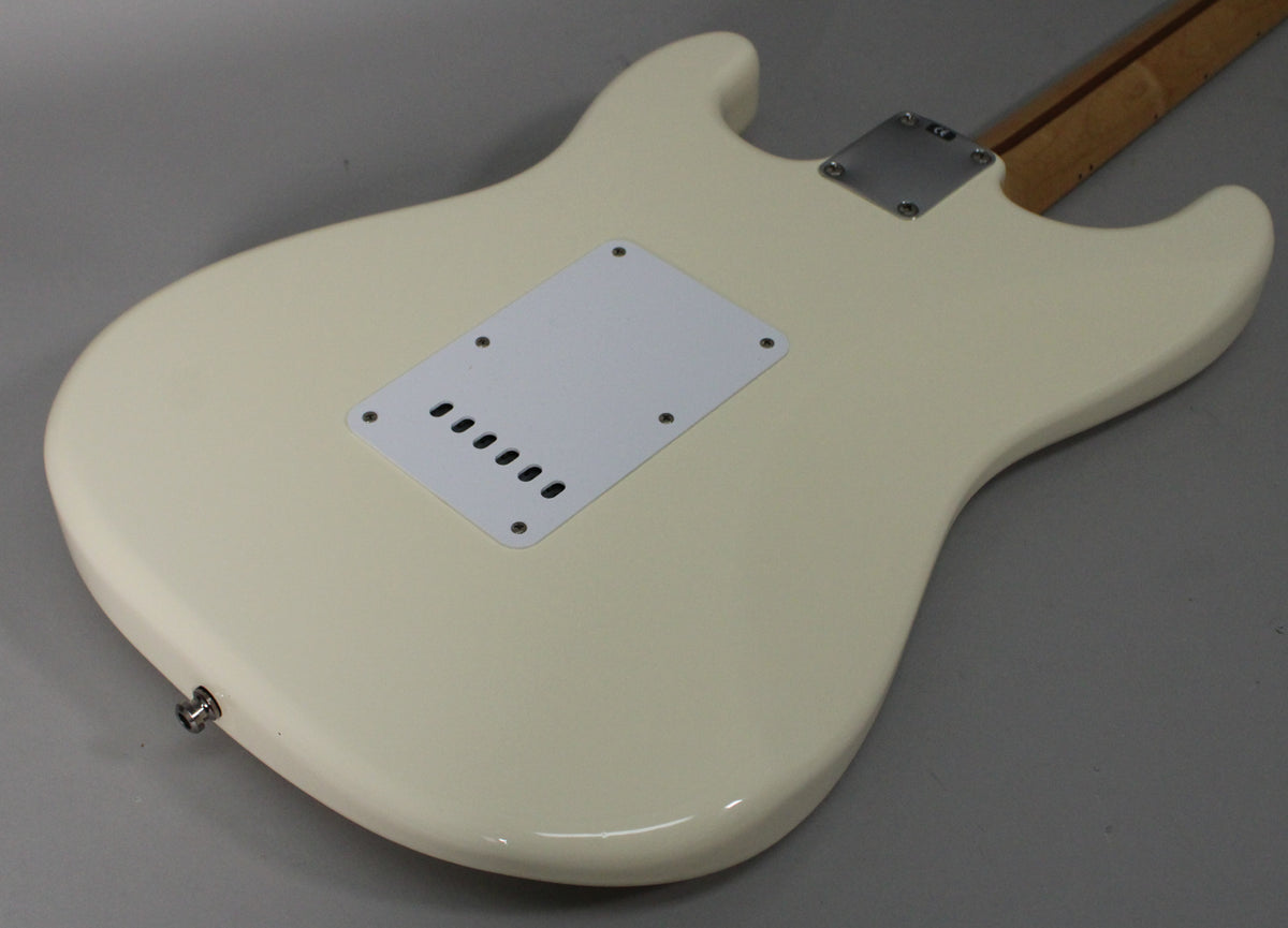 The back of an Olympic White Stratocaster body, angled from the lower bout, showing the tremolo cavity cover and output jack.