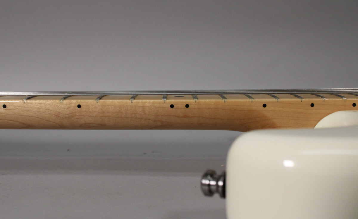 Close-up of the light maple neck and fretboard with black dot inlays, showing the Olympic White body in the foreground.