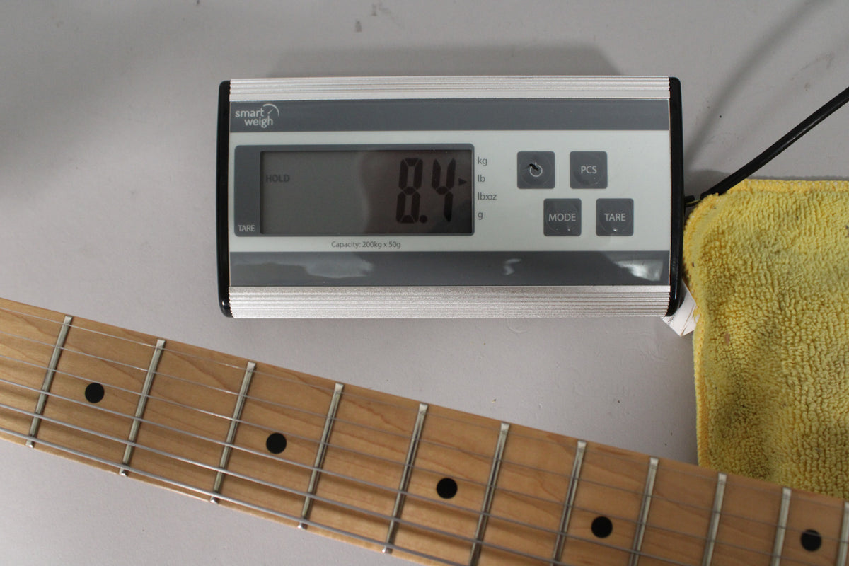 A digital scale displays "8.4" in kg, with a maple fretboard and black dot inlays visible below.