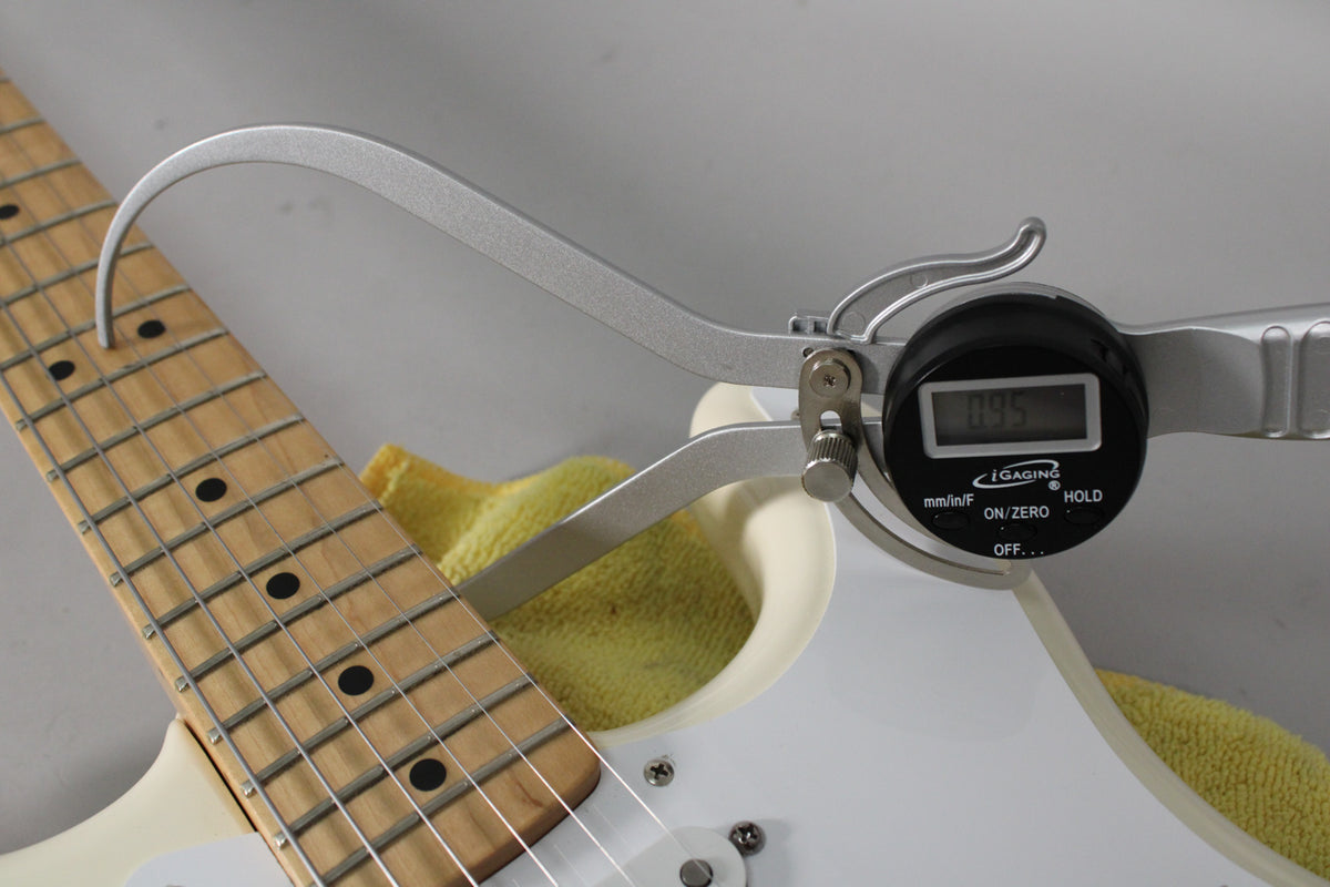 A digital caliper measures the Olympic White Stratocaster's fret height at 0.95mm, with a maple fretboard and black dot inlays visible.