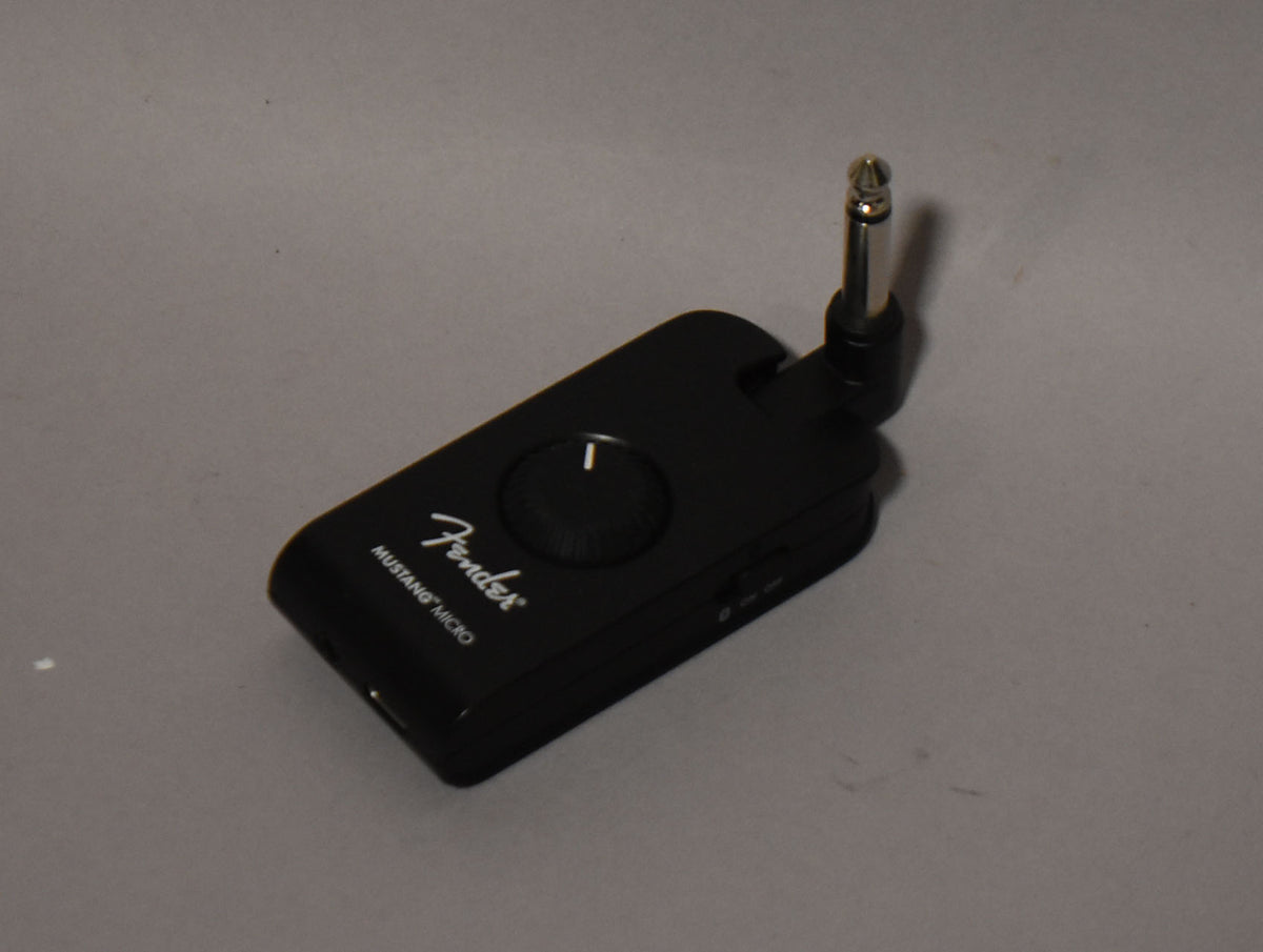 The black headphone amp is angled from above, showing its top with a large volume knob and a silver jack pointing upwards.