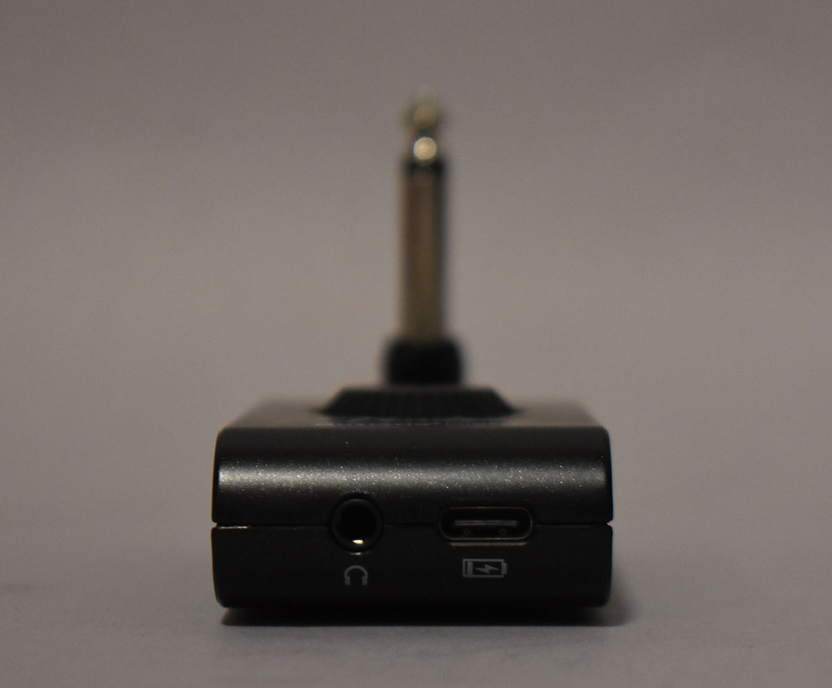 The black headphone amplifier is viewed from the front, showing a headphone jack, a USB-C port, and a guitar jack.