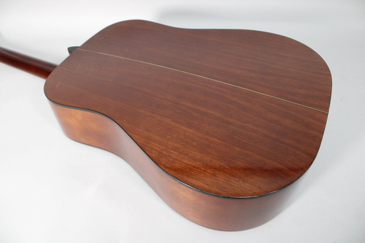 The acoustic guitar's dark brown back and sides are visible from the lower bout, showing light scratches and a center seam.