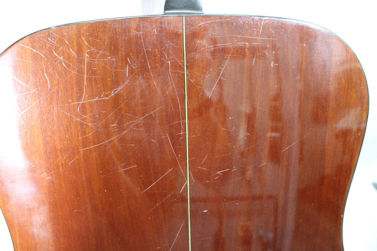 The guitar's dark brown back, viewed from above, shows many light scratches and a thin, light-colored vertical seam down the center.