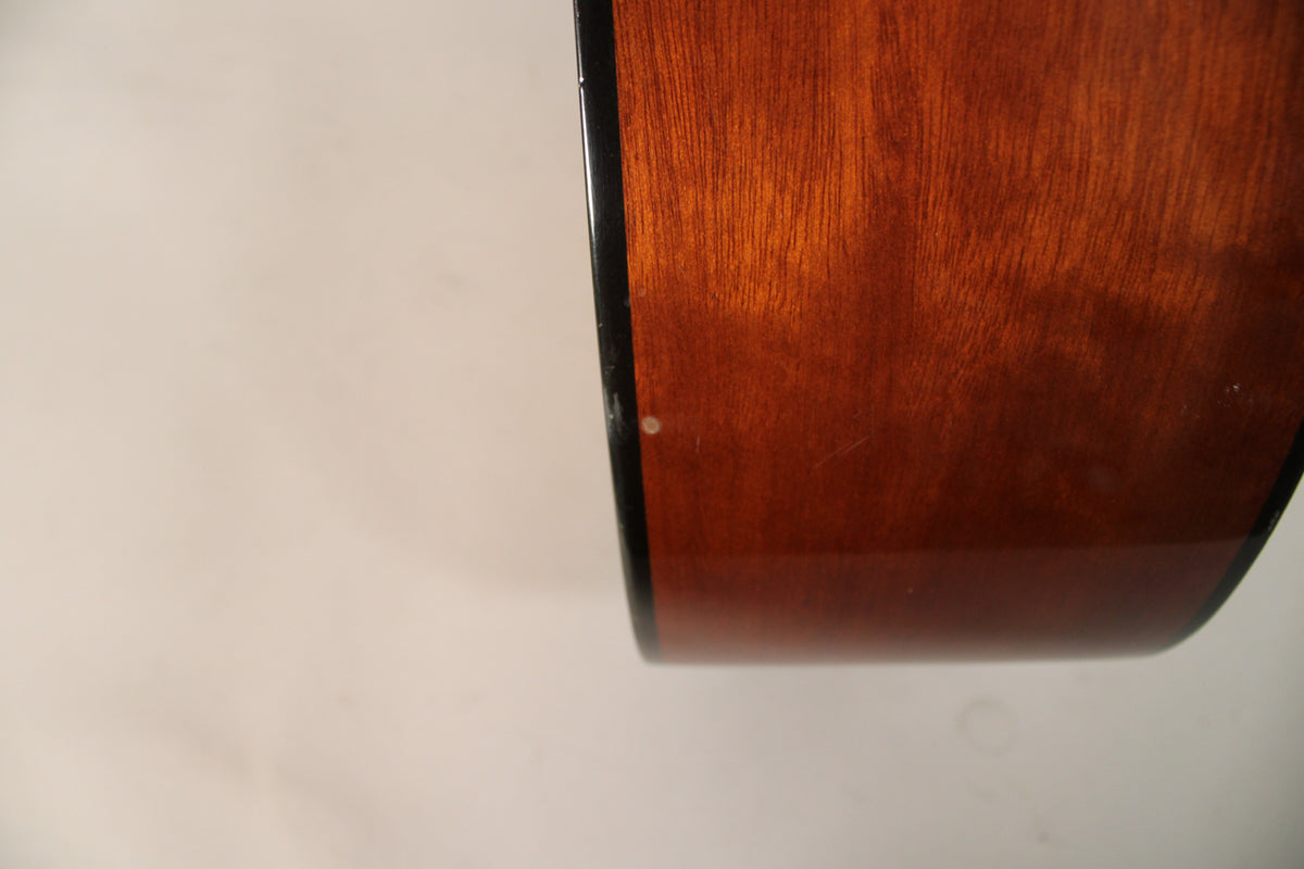 Close-up of the guitar's dark reddish-brown side with a black binding, showing a small white ding and light scratches on the finish.