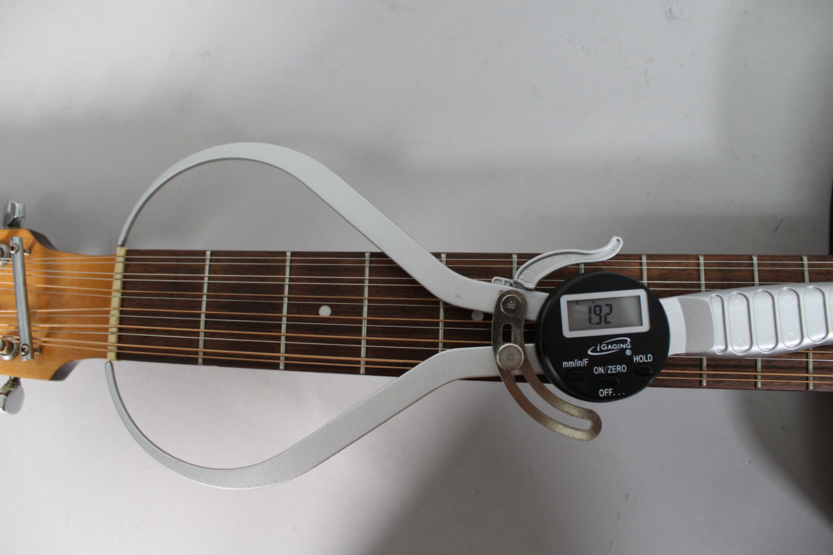 A digital caliper measures the neck width of the 12-string acoustic guitar, showing "1.92" on its display.
