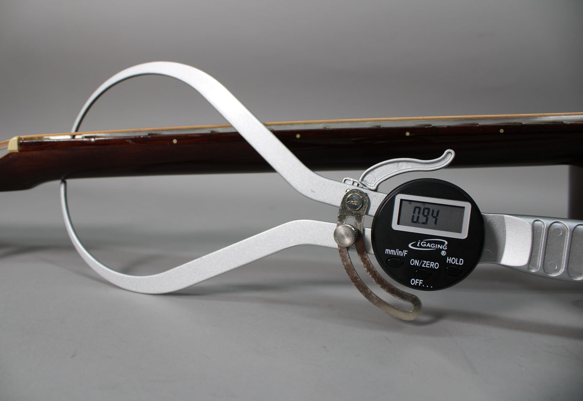 A digital caliper measures the dark brown neck and fretboard, showing a reading of 0.94.