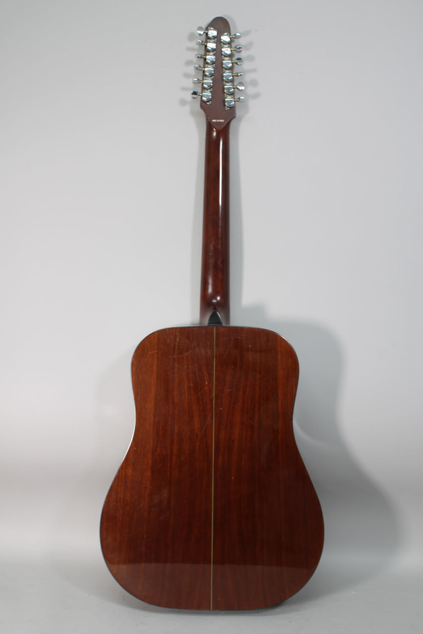 The guitar's dark brown back and neck are visible, with light scratches on the body and 12 chrome tuners on the headstock.