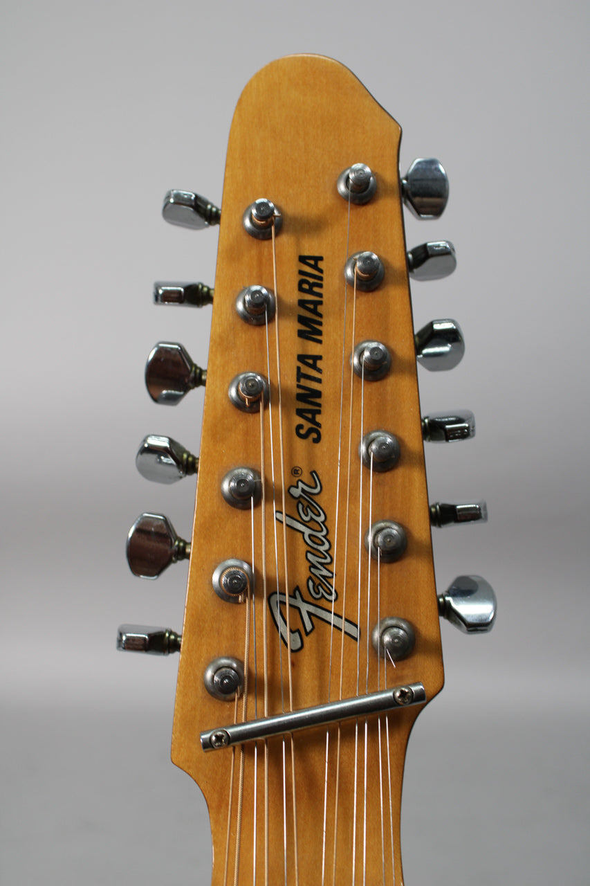 The 12-string acoustic guitar's headstock is shown from the front, with a natural wood finish and chrome tuners.