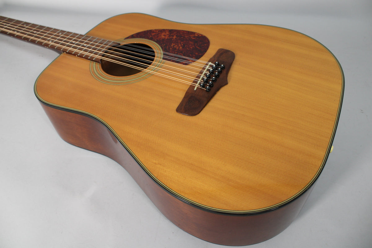 The 12-string acoustic guitar's light-colored top, dark pickguard, and dark bridge are angled from the upper left.