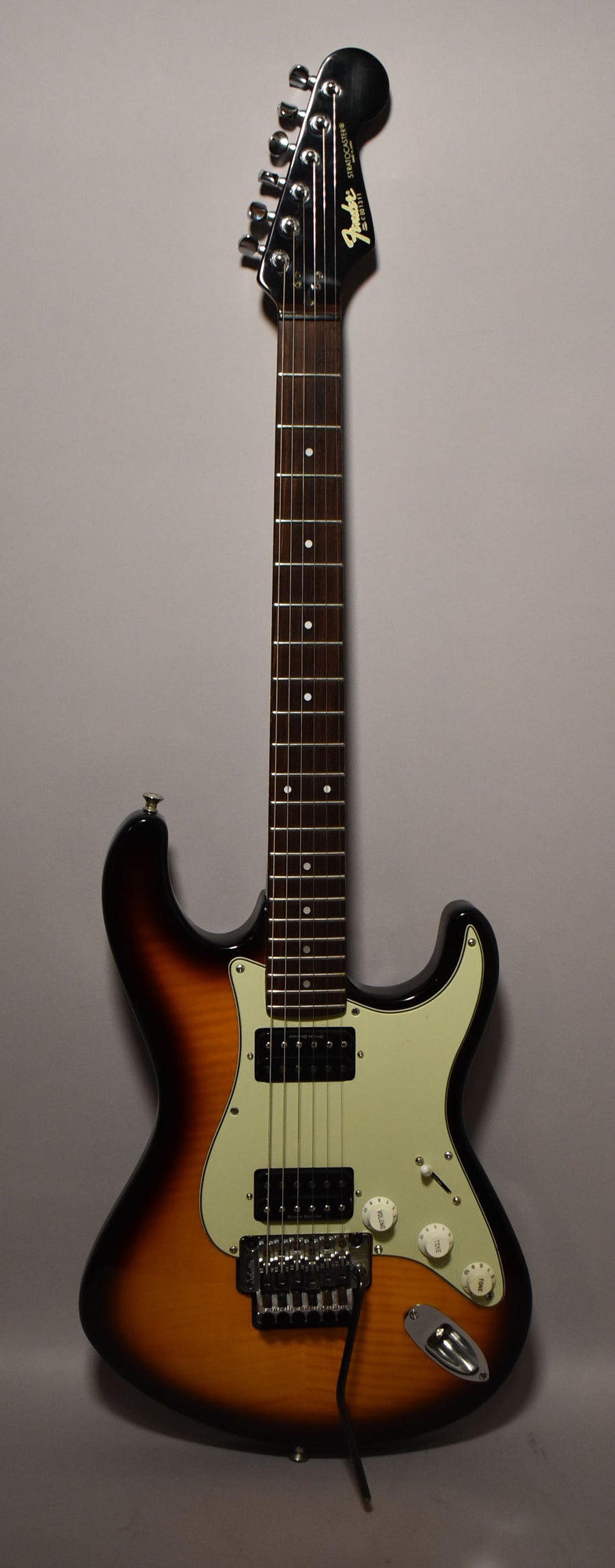 Full-length view of a sunburst S-style guitar with a cream pickguard, two humbuckers, a Floyd Rose tremolo, and white control knobs.