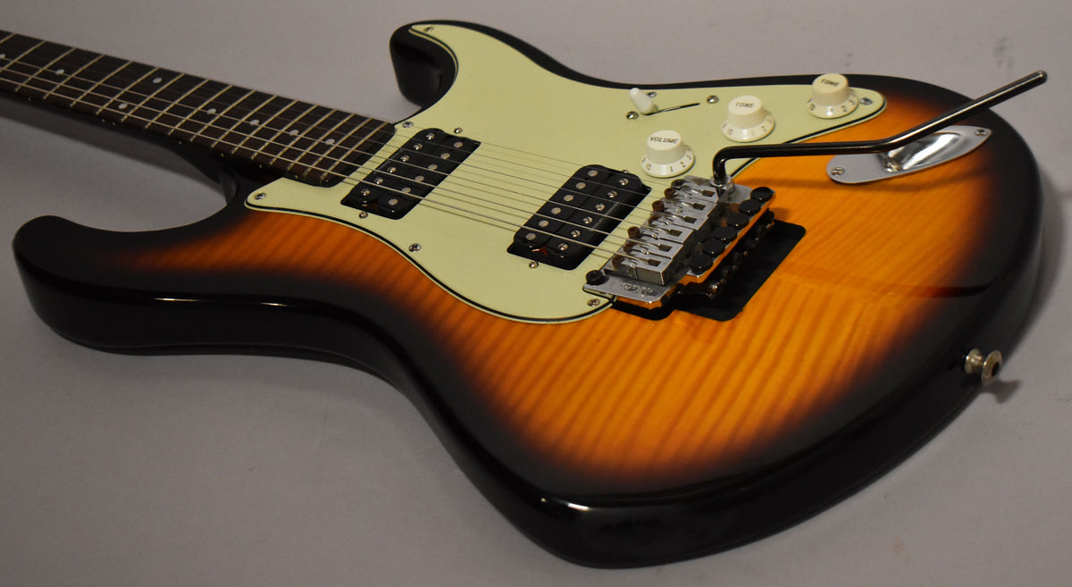 The sunburst guitar body, with a flame maple top, is angled from the neck to the lower bout, showing the cream pickguard and black humbuckers.