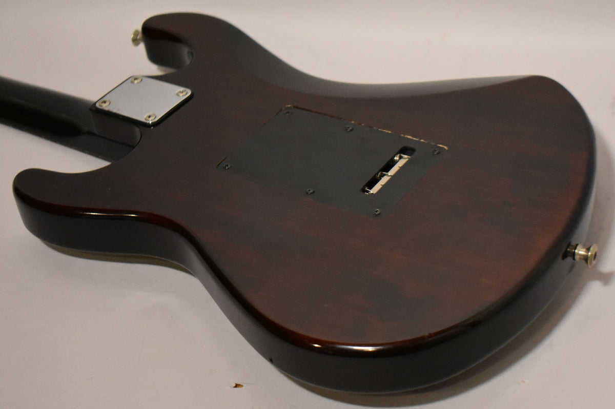 The back of the dark sunburst guitar body shows a black tremolo cavity cover with a missing section, and a chrome neck plate.