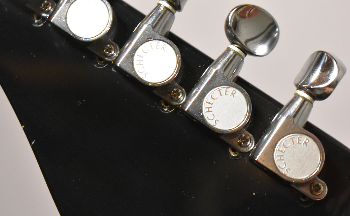 Close-up of the black headstock's rear, showing three chrome tuners with white buttons, some minor scratches, and dust.