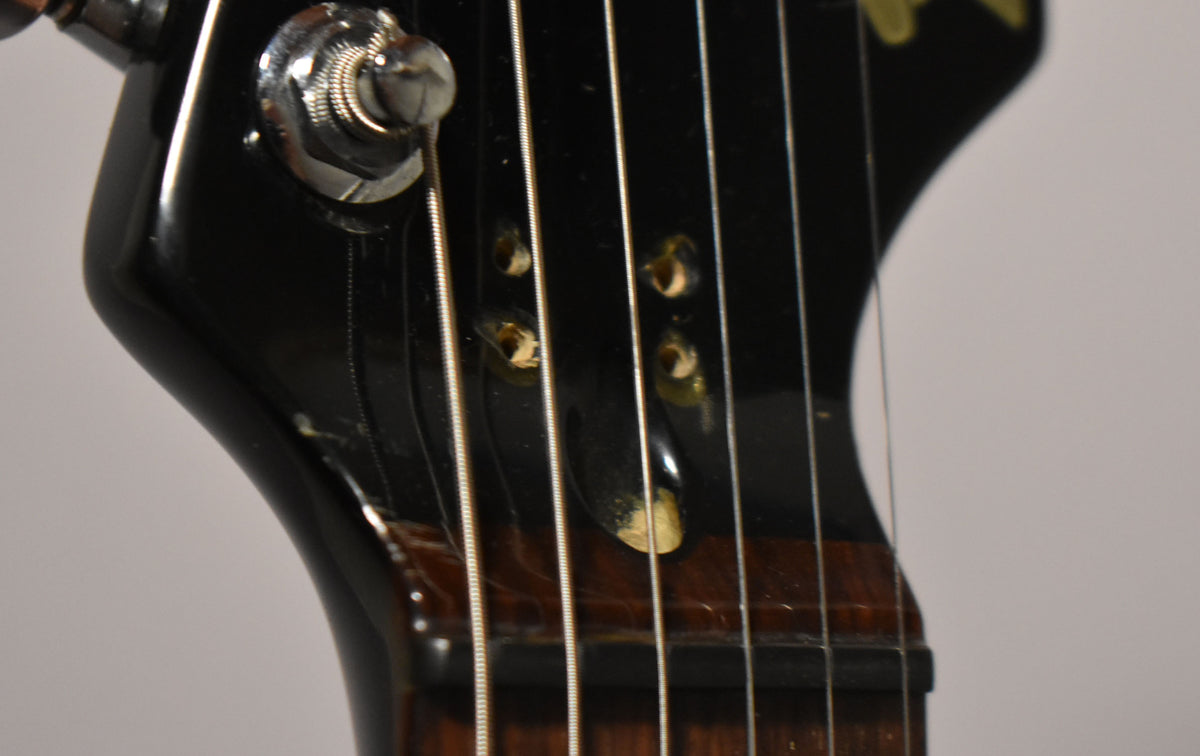 Close-up of the black headstock, showing a chrome tuning peg, string tree, and three string holes with visible wear around them.