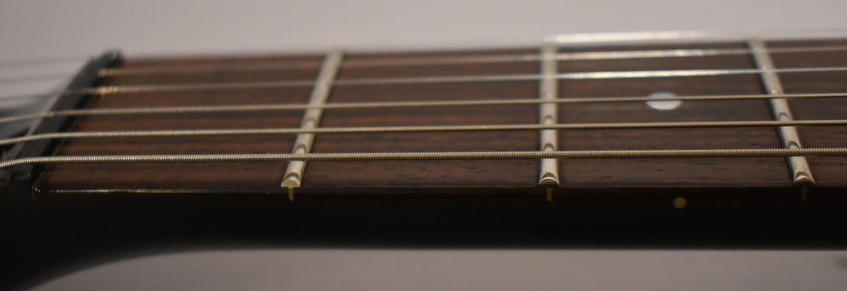 Close-up of the dark rosewood fretboard with light wear, showing the nut and first five frets with dot inlays and light strings.