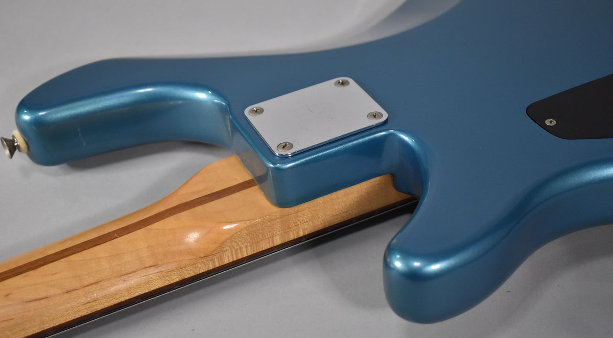 The bass's Lake Placid Blue body and neck plate are shown from the back, with the light maple neck visible below.
