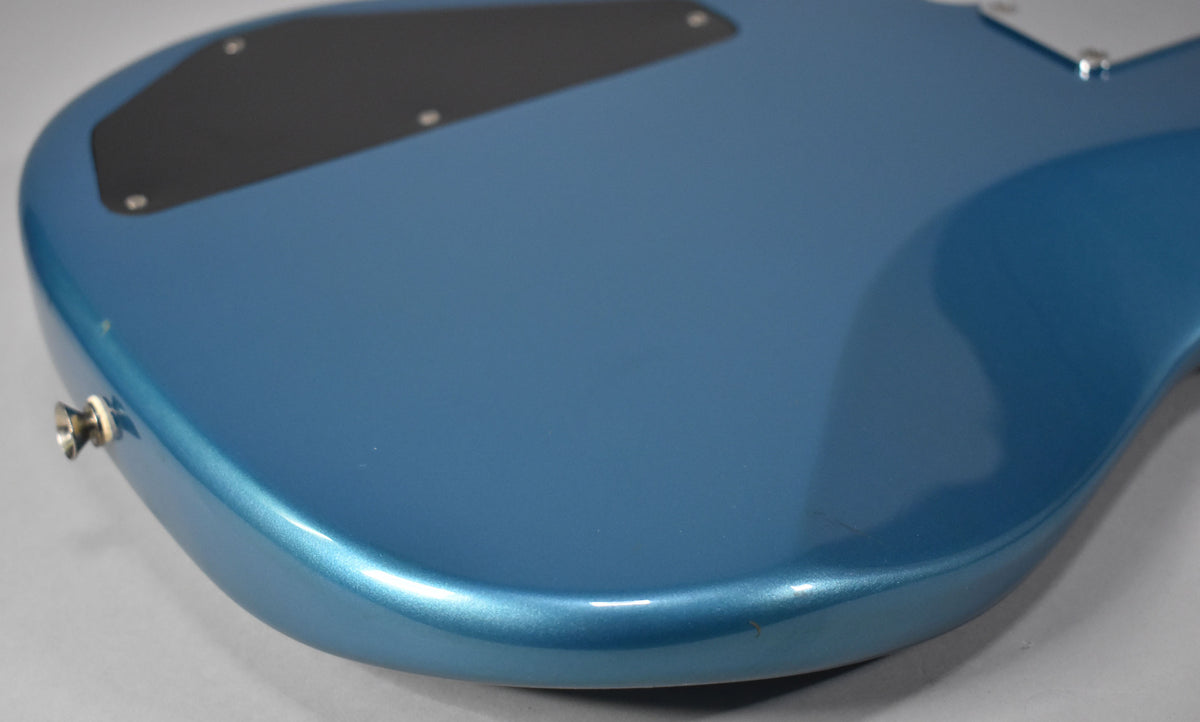The bass's Lake Placid Blue body, with a metallic sheen, shows a black control plate and a chrome strap button.