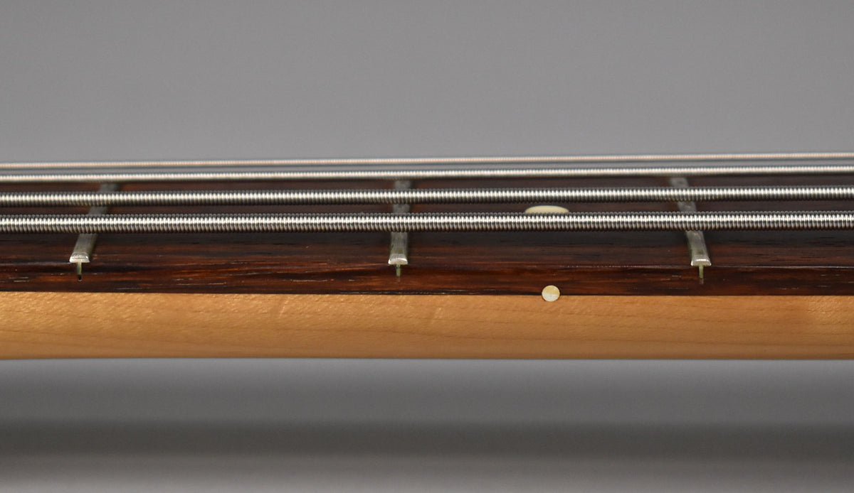 Close-up of the bass neck, showing the dark rosewood fretboard, light maple neck, and four strings with a single round side dot.