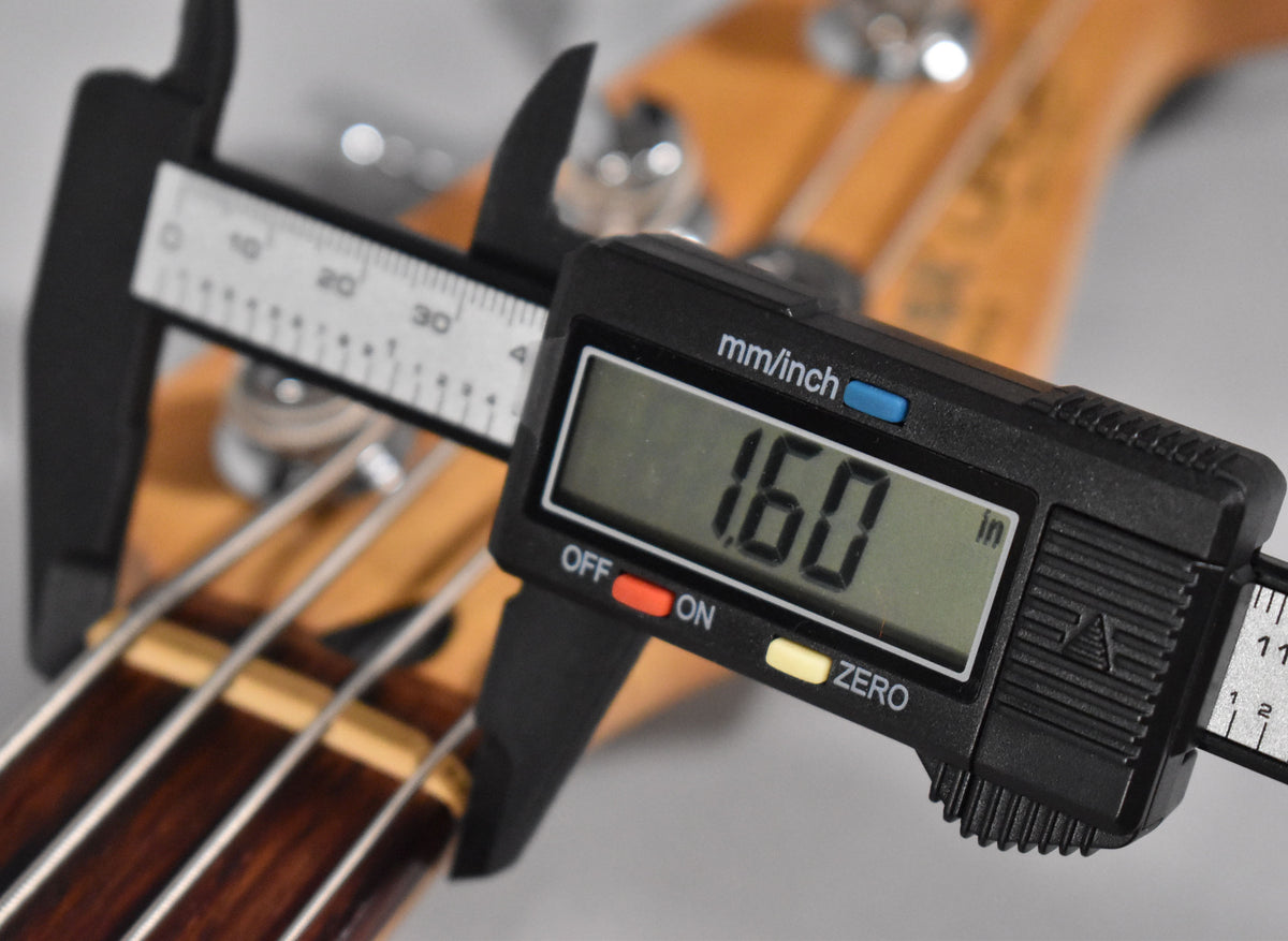 A digital caliper measures the bass nut width at 1.60 inches, with the dark rosewood fretboard and light maple neck visible.