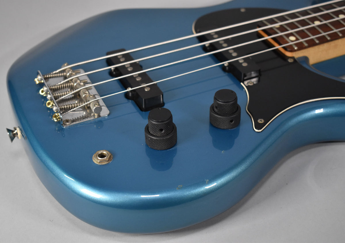 Close-up of the Lake Placid Blue bass body, showing the bridge, two black stacked knobs, output jack, and a few small dings.