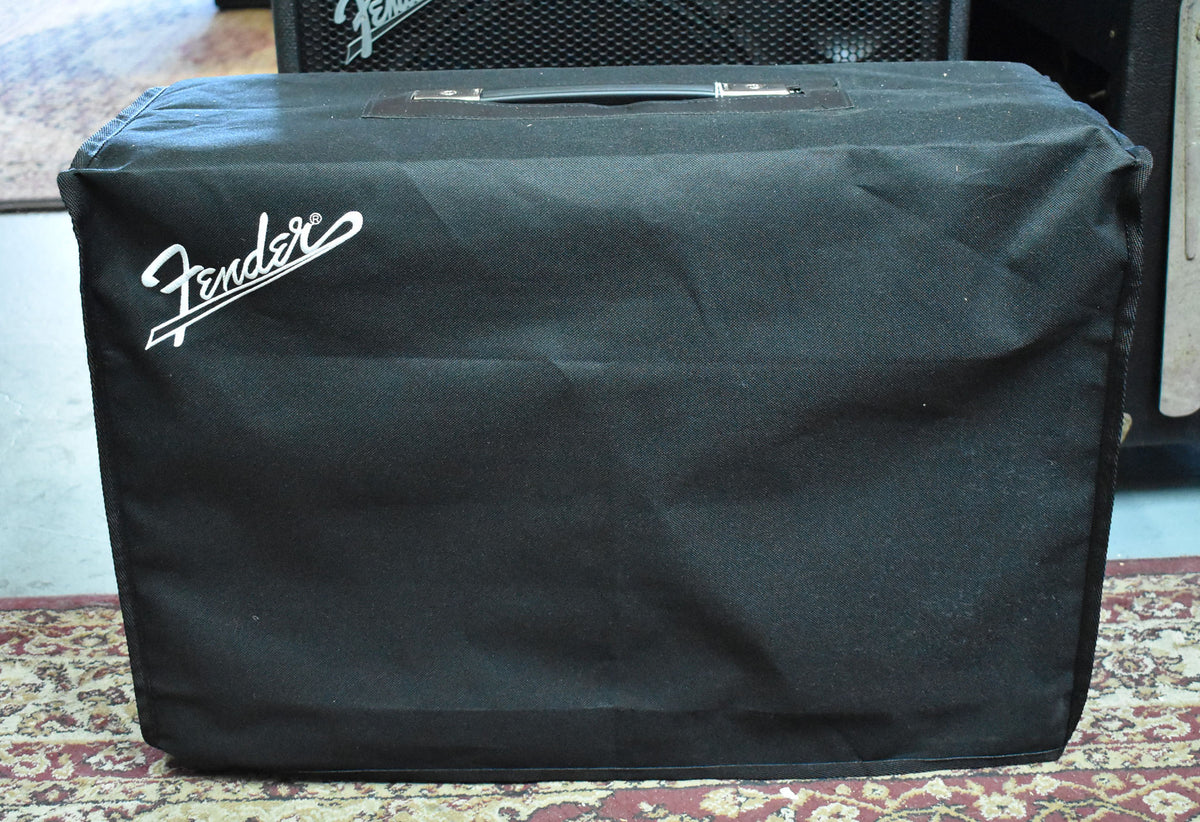 The black amplifier is covered by a black fabric cover with a white logo, showing a top handle and some wrinkles.