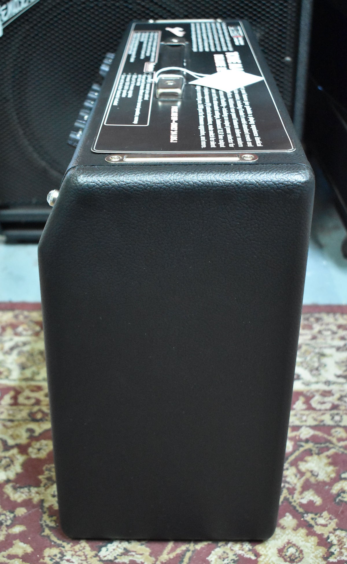 The black textured amp is viewed from the right side, showing the top panel with a chrome handle and white information stickers.