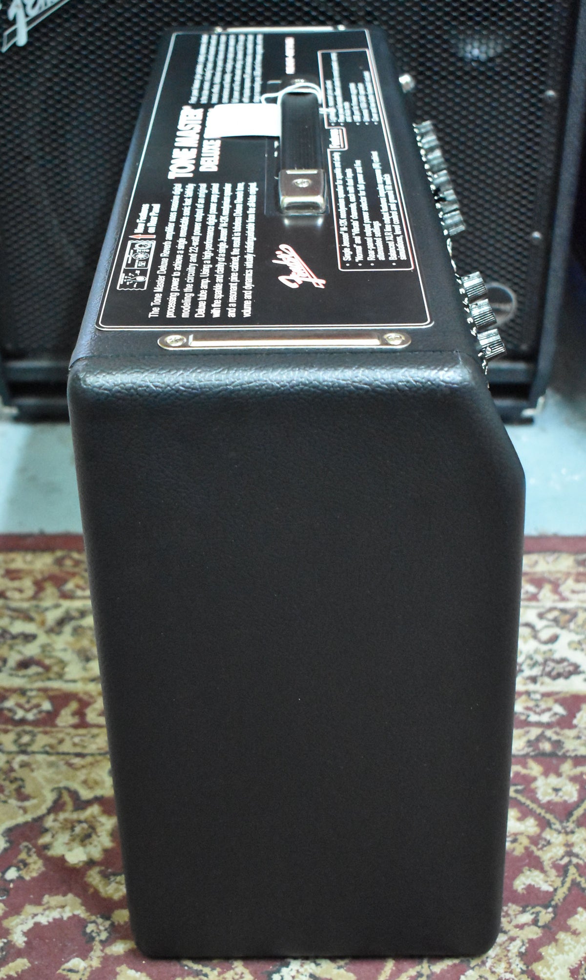 A black combo amp, viewed from the right side, showing the top panel with a handle and text, and a row of silver knobs.