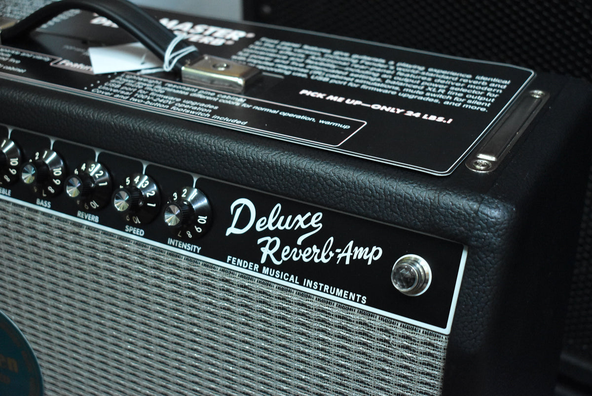 Close-up of the black textured amp's top and front panel, showing the carry handle, silver control knobs, and a gray grille cloth.