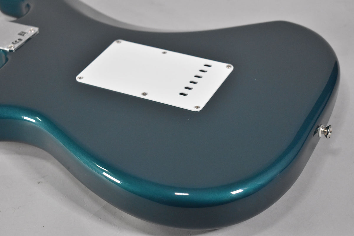 The guitar's ocean turquoise back shows a white tremolo spring cover with six slots, and a chrome output jack.